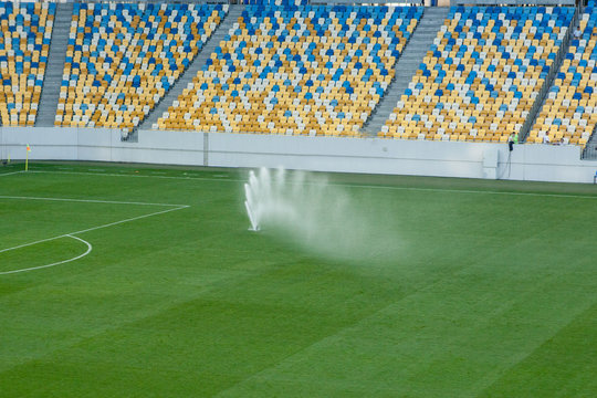 Automatic lawn grass watering system at the stadium. A football, soccer field in a small provincial town. Underground sprinklers spray jets water