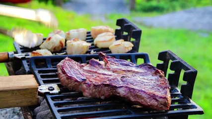 Steak and Scallops grilling on a Hibachi as smoke and flames develop from hot charcoal on a sunny summer evening