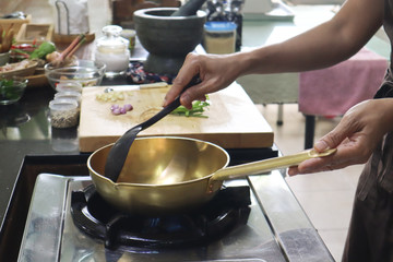 a lady cooking Thai food with brass wok 