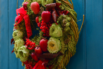 Wreath with red apples, berries and roses hanging on a blue door.