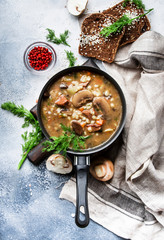Autumn or winter meat vegetable mushroom hot soup with beef and wholegrain barley. With black breaв and parsley, top view, gray kitchen table, copy space
