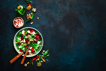 Arugula, Beet and cheese salad with fresh radicchio and walnuts on plate with fork, dressing and spices on blue kitchen table background, place for text, top view