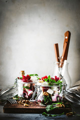Fototapeta na wymiar Beet and cheese healthy salad with arugula and walnuts, trendy salad jar, gray kitchen table, place for text, selective focus
