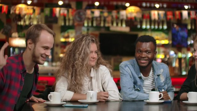 Student meeting in a restaurant and cafe. A man in a shirt tells a story to friends, two girls and an African American are listening and laughing. A group of friends spend time together.