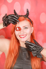 Fashion pretty young woman with red lollipop heart wearing black leather dress and devil horns