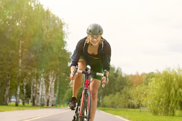 Fototapeta na wymiar Sportswoman in uniform and helmet riding on the bike path on the background of green trees