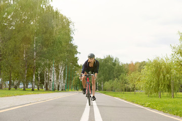 Sportswoman in uniform and helmet riding on the bike path on the background of green trees
