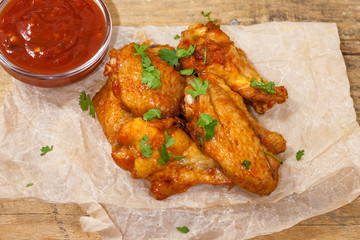 Fried juicy chicken wings marinated with honey, soy sauce, spices, sprinkled with finely chopped cilantro on a paper background. Asian recipe, top view, close-up.