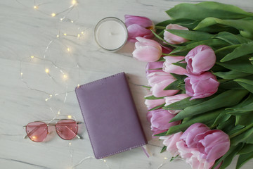 Glasses, tulips and accessories in pink color on white wooden table.
