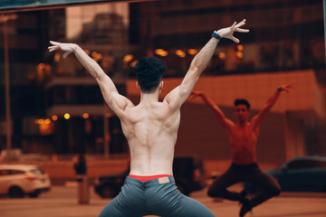 Young male ballet dancer on a building background with mirror reflextion. Outdoor dance.