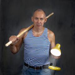 A man with a stick in one hand and a luminous yellow table lamp in the other hand.