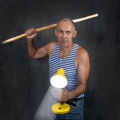 A man with a stick in one hand and a luminous yellow table lamp in the other hand.
