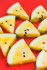 a lots of triangular pieces of ripe yellow watermelon on red background
