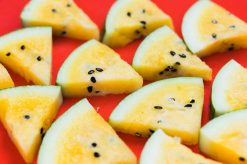 a lots of triangular pieces of ripe yellow watermelon on red background