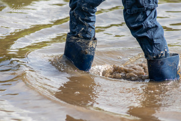 Kind mit blauer Hose und blauen Gummistiefeln watet nach einer Überschwemmung wegen Deichbruch...