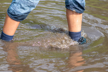 Junge watet mit nassen Schuhen und nassen Socken durch Hochwasser nach einer Überschwemmung mit starkem Regen und Deichbruch