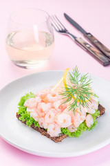 Traditional savory swedish sandwich with a dark bread, lettuce, eggs, mayonnaise, shrimps, dill and lemon, on pink background, vertical