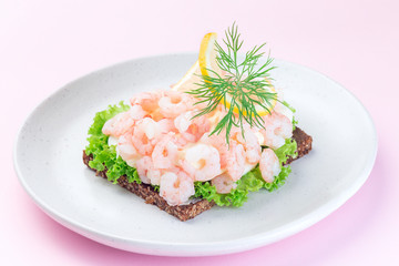 Traditional savory swedish sandwich with a dark bread, lettuce, eggs, mayonnaise, shrimps, dill and lemon, on  pink background, horizontal