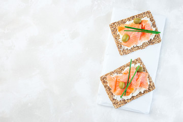 Sandwich with smoked salmon and cream cheese on thin multi seed  crispbread, garnished with green onion and olives,  horizontal, top view, copy space