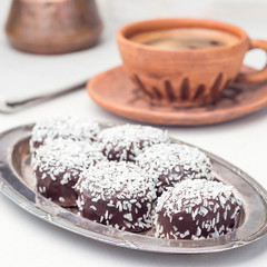 Swedish sweets chocolate balls or chokladbollar, made from oats, cocoa, butter and coconut, on a metal plate, served with coffee, square format