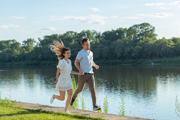 Summer nature, relationship and people in love concept - happy couple running near the lake