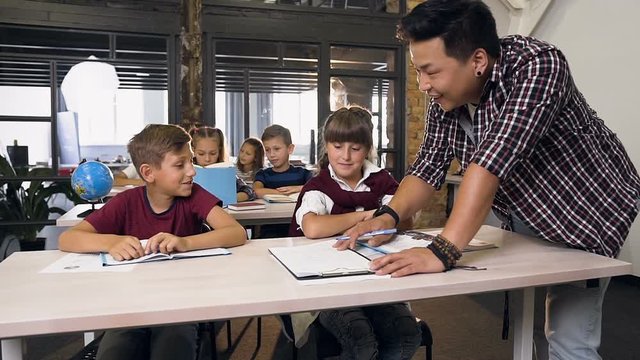 Young male Korean teacher helps elementary pupils to learning lessons in class