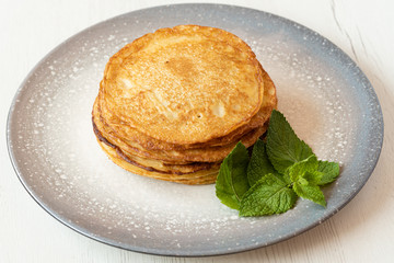 Stack of American pancakes with some mint leaves in a gray plate on a wooden table. cooking concept.