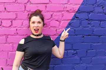 Cheerful positive young woman in goth clothing posing against a blue-purple brick wall with copyspace. The concept of positive advertising content.