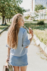 Summer city lifestyle girl portrait. Stylish young woman with ice cream in a waffle cone in her hand on a sunny summer hot day