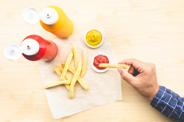 Fototapeta na wymiar Top view of youngman enjoy eating with french fried and dipping sauce ( mustard,ketchup ) on wood table background