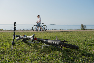 Report from the seashore. The bicycle lies on a green grass. People walk along the water. Summer. Sunny day.