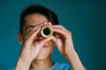 Close up of smiling boy looking at spyglass on blue background