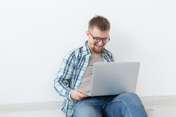 Positive young man in casual clothes and glasses surfing the Internet using Wi-Fi and a laptop in search of rental housing. Housewarming and apartment search concept.
