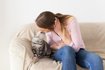 Obraz premium Woman at home kissing her lovely fluffy cat. Gray tabby cute scottish fold cat. Pets and lifestyle concept.