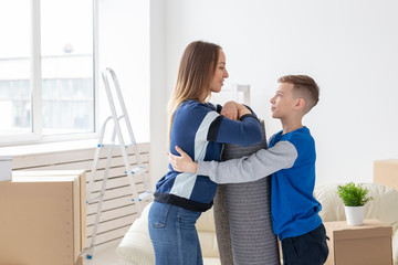 Relocation, housewarming and real estate concept - Smiling single mother and a charming son are holding a folded carpet in a new living room intending to spread it in a new apartment