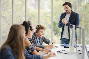 Young people operator team with headsets are working and training by the boss in a call center....