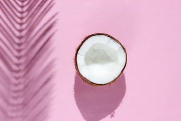 Minimalistic tropical still life. Two halves of chopped coconut with shadows from palm leaves on pink background. Creative fashion concept. Top view.