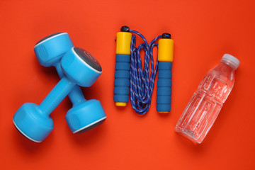 Naklejka premium Flat lay style sport concept. Dumbbells, jump rope, bottle of water. Sports equipment on orange background. Top view