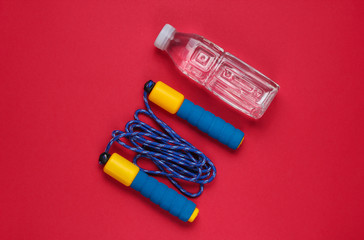 Flat lay style sport concept. Jump rope, bottle of water. Sports equipment on red background. Top view