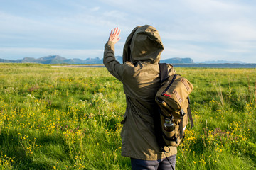 Girl in jacket with a hood and backpack enjoys scenic view. Beautiful nature landscape. Green grass, mountain. Lonely women. Enjoy moment, relaxation. Wanderlust. Travel and adventure. Explore Norway