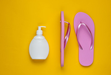 Beach accessories. Fashionable beach pink flip flops, sunblock bottle on yellow paper background. Flat lay. Top view