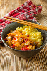 Saffron rice with pieces of chicken and vegetables on wooden table.