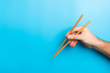 Creative image of wooden chopsticks in male hands on blue background. Japanese and chinese food with copy space