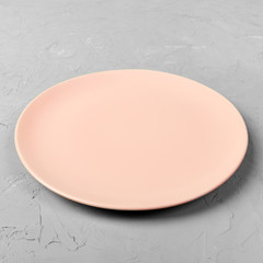 Empty pink or coral round plate on grey cement table background. Top view, template for your design