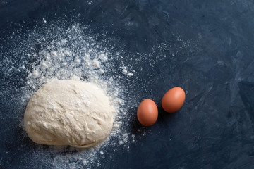 Flat lay composition of a ball of raw baking dough and two brown eggs with dust of wheat flour on a...