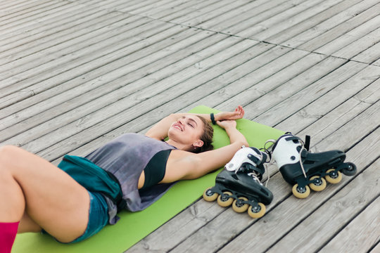 Tired but happy woman roller skater resting lying on mat outdoors