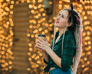 An informal young woman with a dreadlocks hairstyle and fashionable summer clothes holds coffee cup...