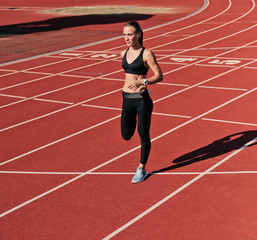 Sprinter woman in sportswear doing warm-up exercises before run on stadium track with red coating...