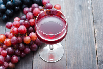 glass of red wine and grapes on black wooden table background