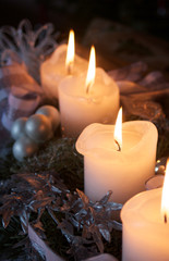 Gesteck mit 4 weißen Kerzen und alle mit Flamme, wärmend weiß und silber